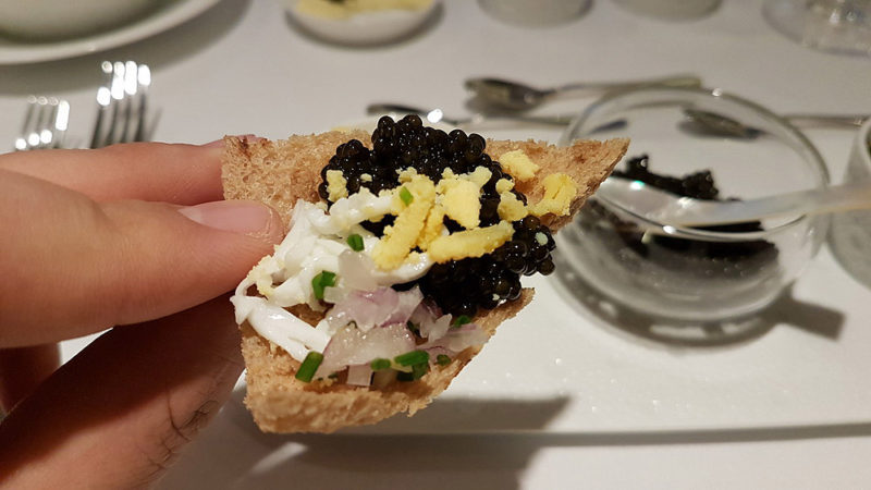 a hand holding a piece of bread with black and white caviar