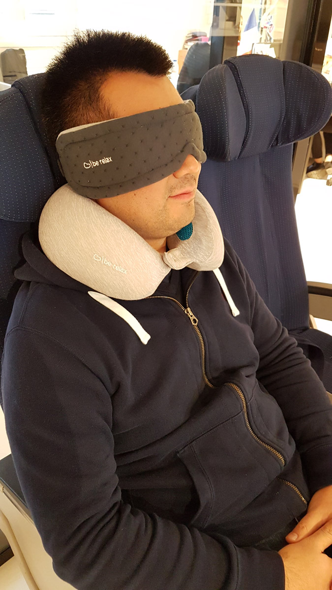 a man wearing a neck pillow and sleeping on a plane