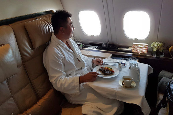 a man in a robe eating food on a table in an airplane