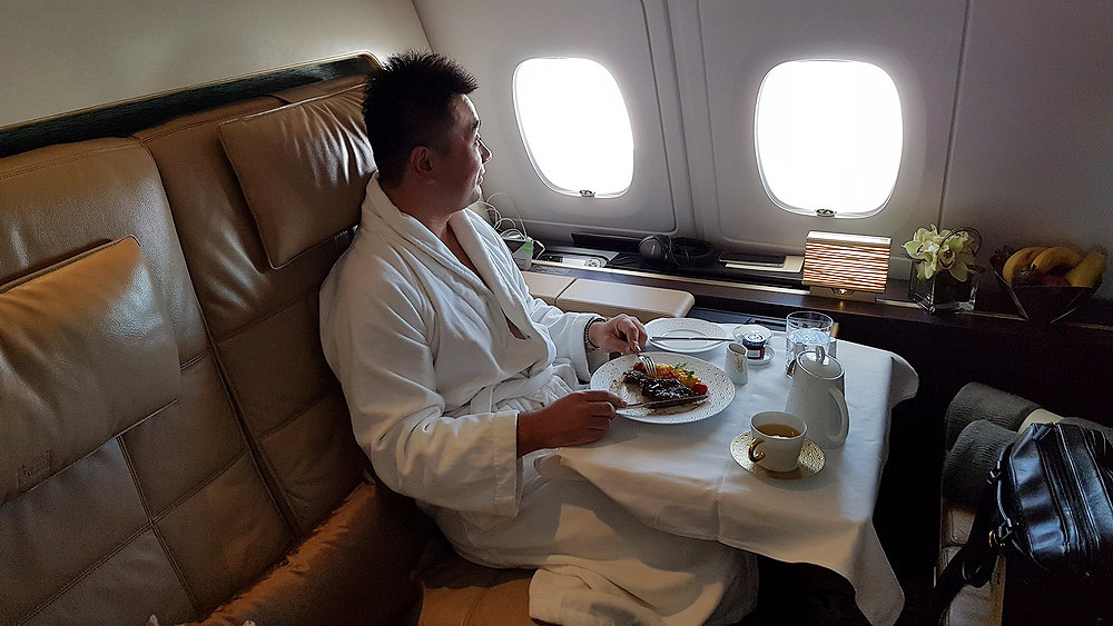a man in a robe eating food on a table in an airplane