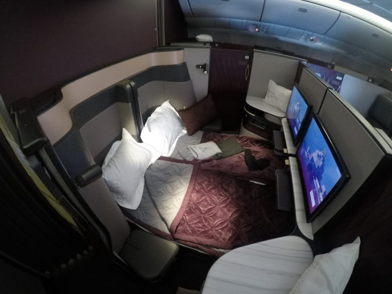 a bed with two pillows and a monitor in the back of a plane