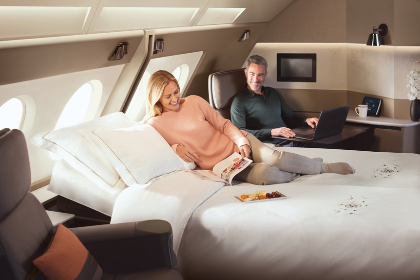 a man and woman sitting on a bed in an airplane