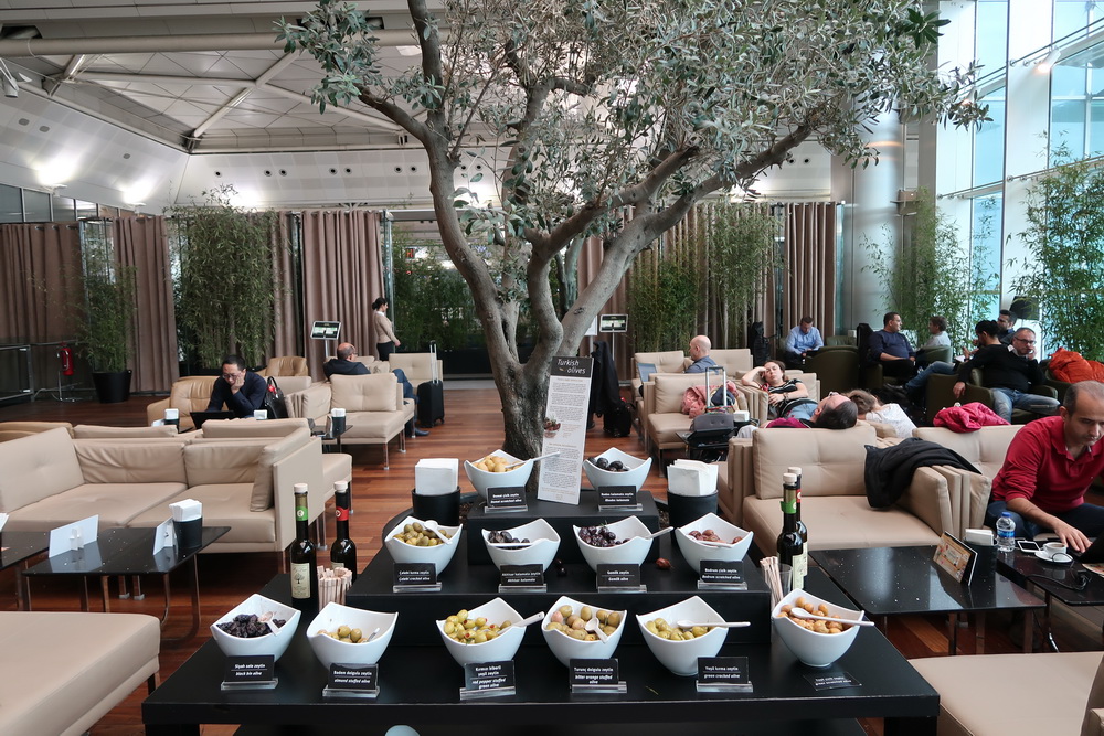 a group of people sitting in a lounge area with a tree and a table with food