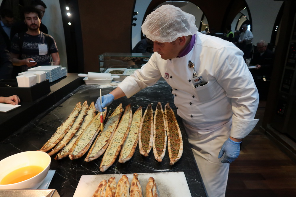 a man in a white coat and hair net standing in a kitchen