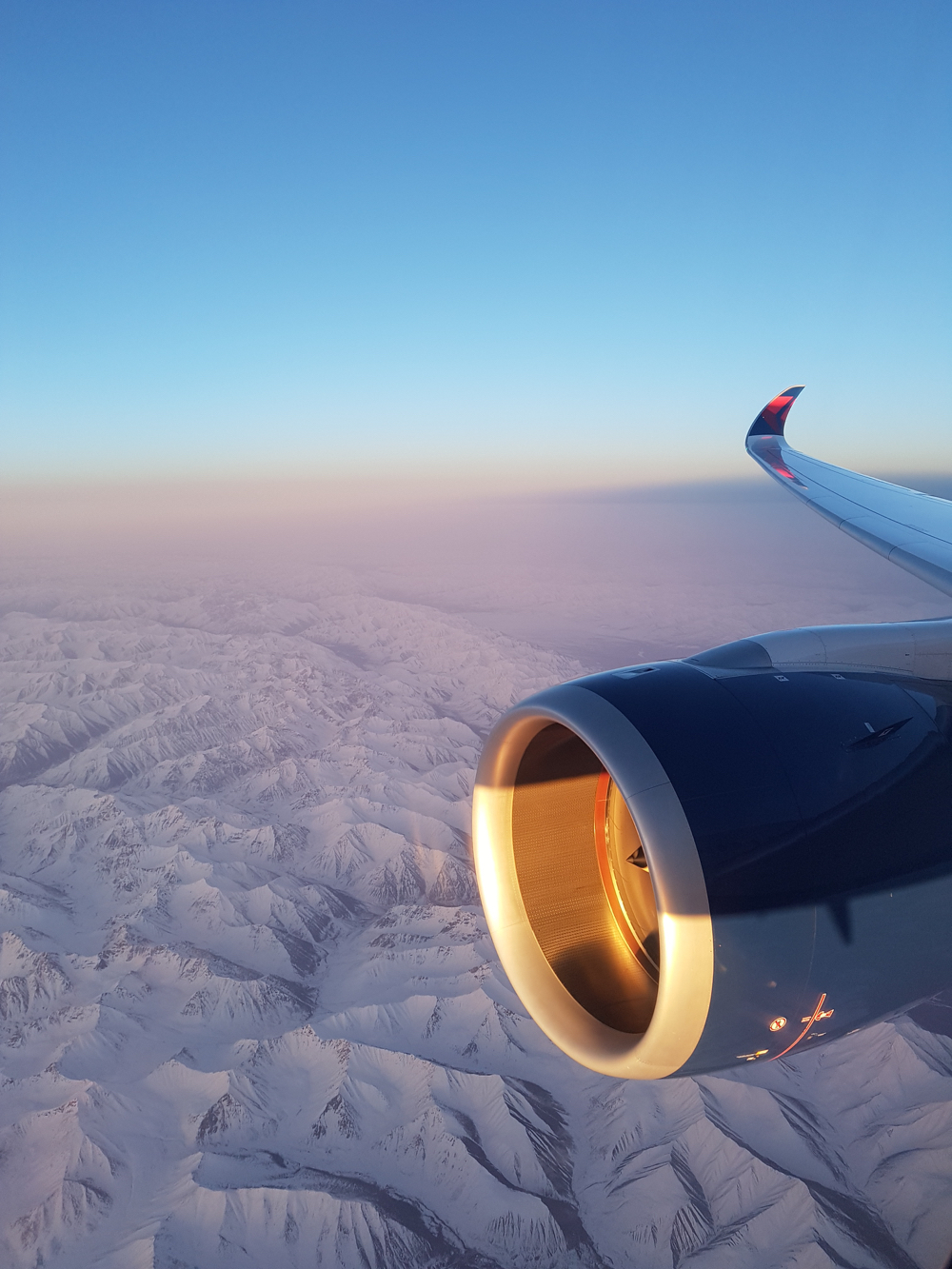 an airplane wing and snow covered mountains