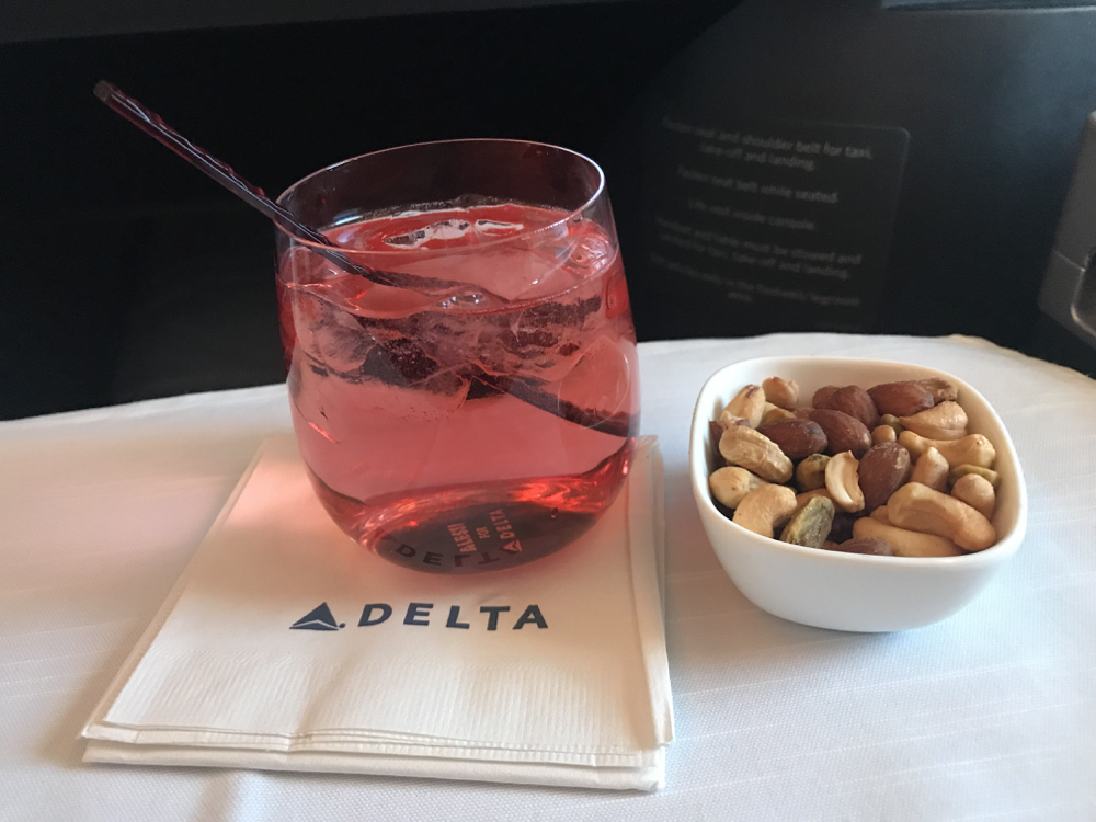 a glass of pink liquid with a spoon next to a bowl of nuts