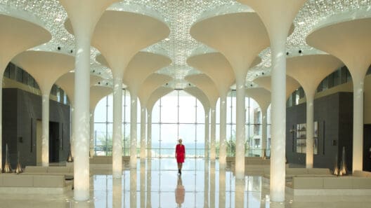 a woman in a red dress in a large room with white columns with Sheikh Zayed Mosque in the background