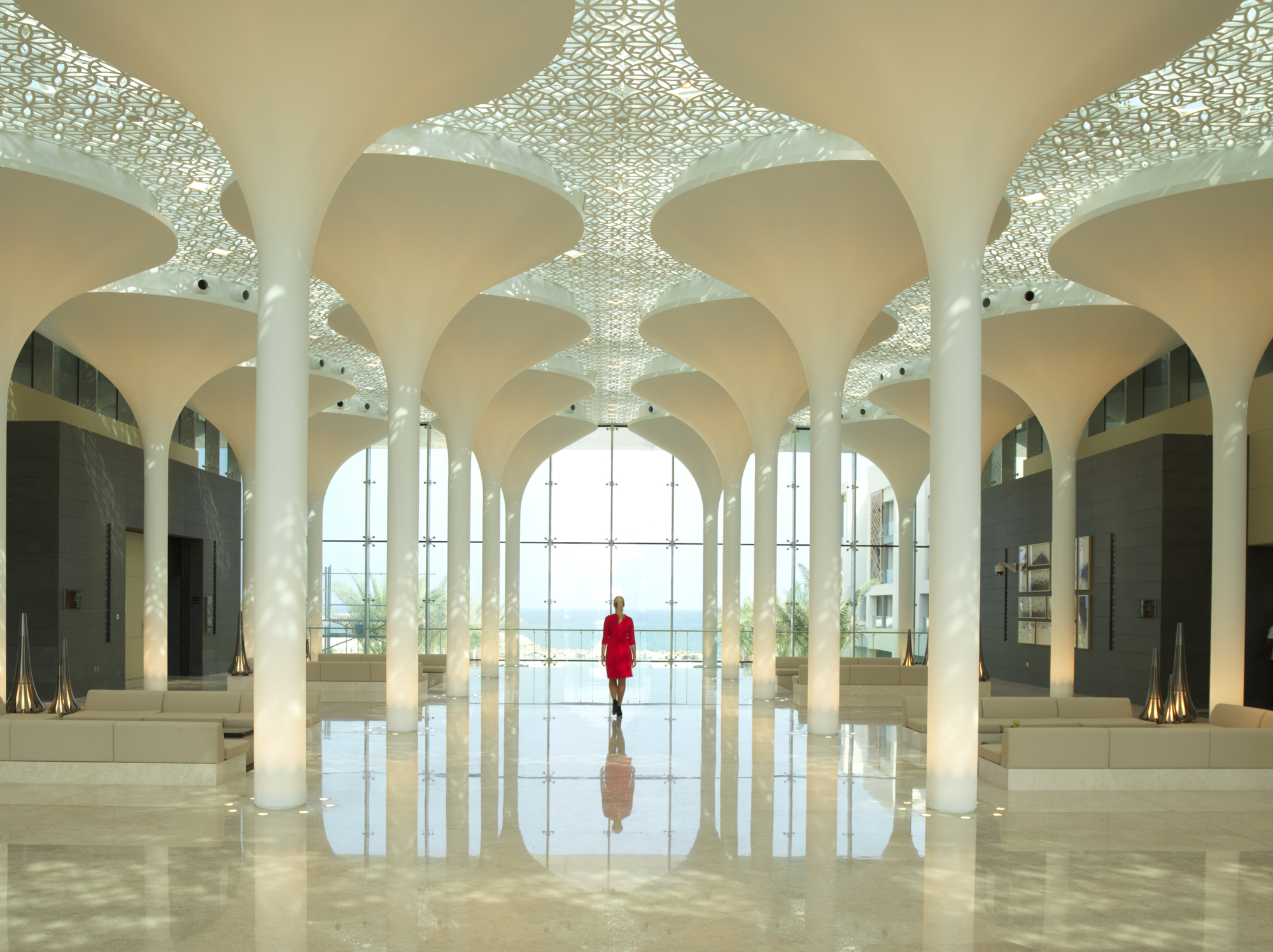 a woman in a red dress in a large room with white columns with Sheikh Zayed Mosque in the background