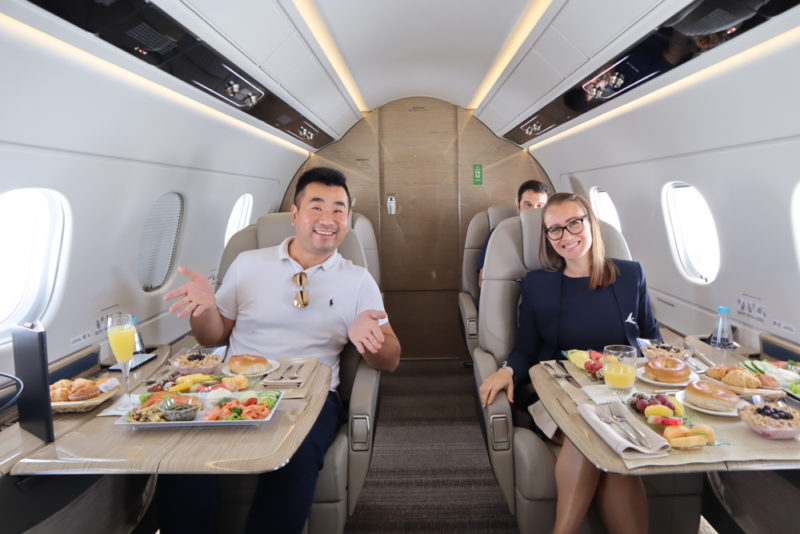 a man and woman sitting in a plane with food on tables
