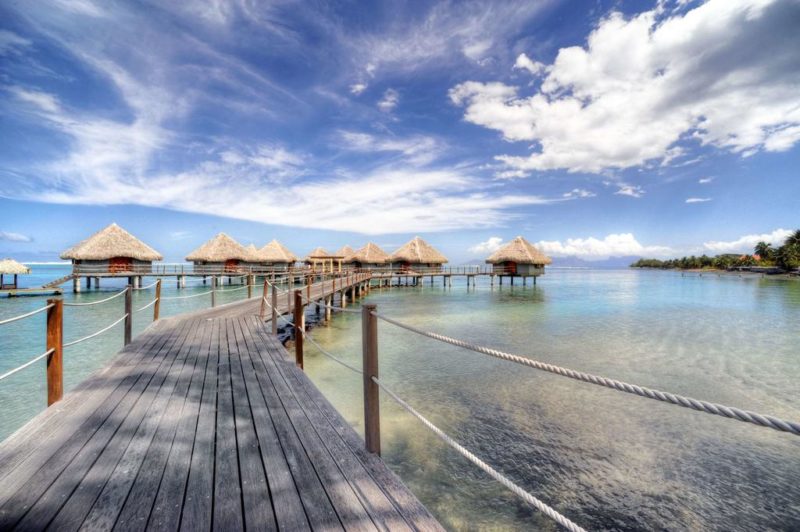 a wooden walkway leading to a row of huts on water