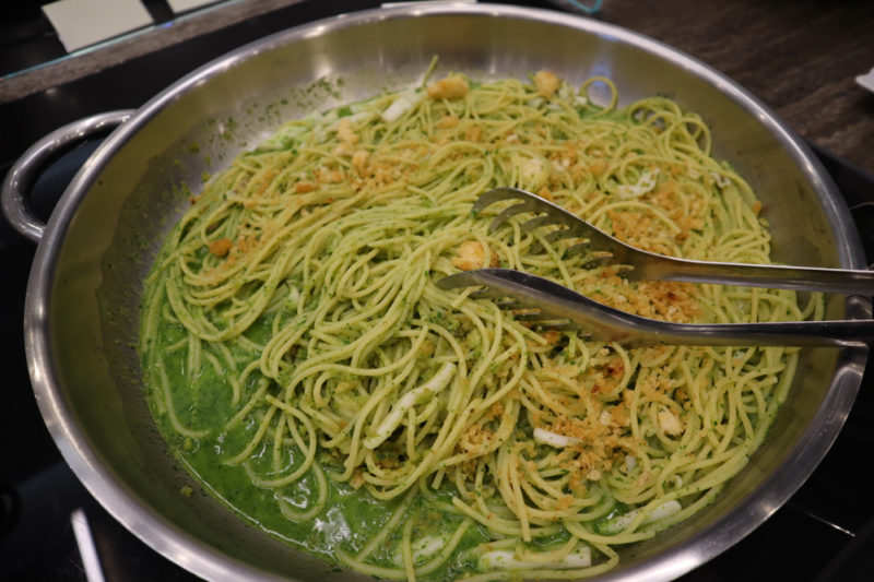 a bowl of spaghetti with green sauce and tongs
