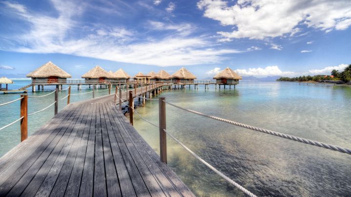a wooden walkway leading to a row of huts on water