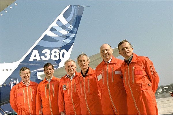 a group of men in orange jumpsuits standing in front of an airplane