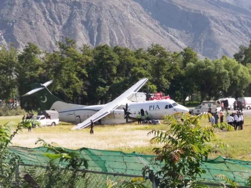 a plane parked in a field with trees and mountains in the background