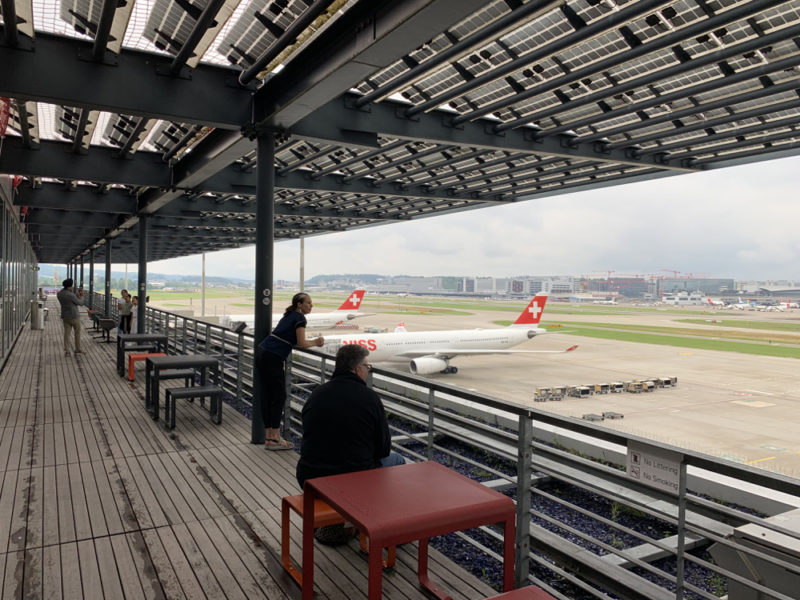 people sitting on a deck with a plane on the runway