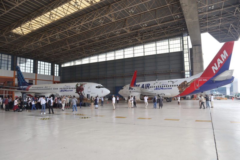 people standing around airplanes in a hangar