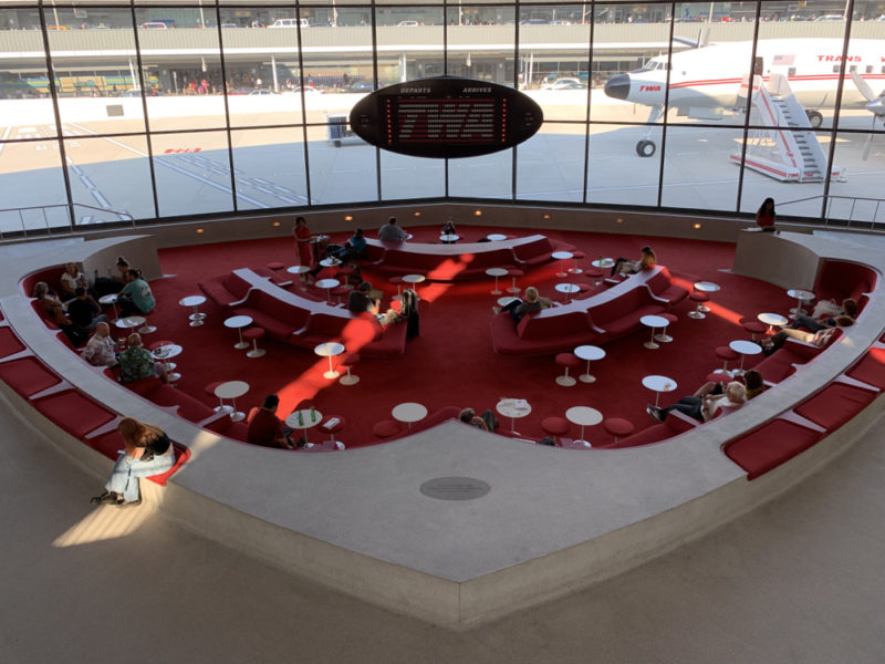 a group of people sitting in a circular area with red seats and tables
