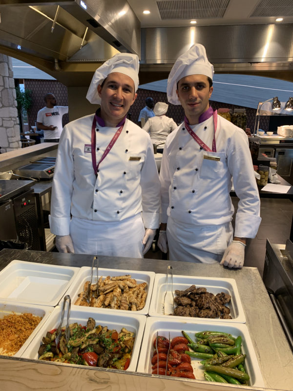 two men wearing chef uniforms standing in a kitchen