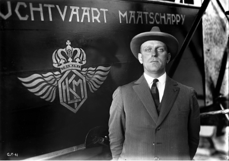 a man in a suit and hat standing in front of a sign