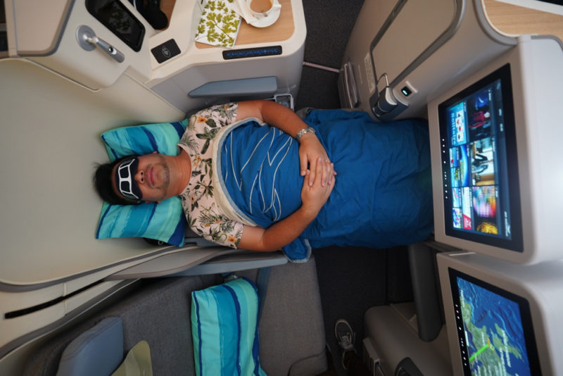 a man in a blue shirt and blue shirt sleeping on a pillow in an airplane