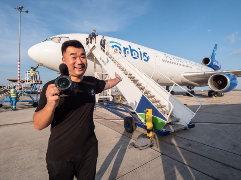 a man holding a camera in front of an airplane