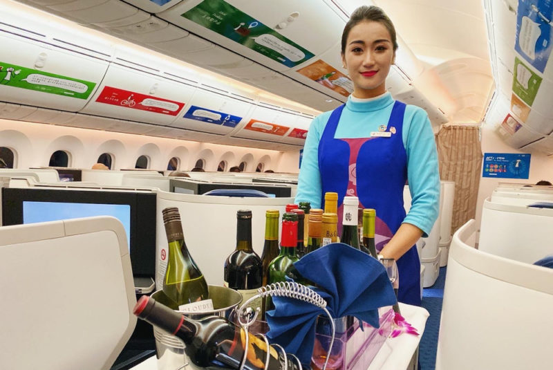 a woman standing in an airplane with a tray of wine bottles