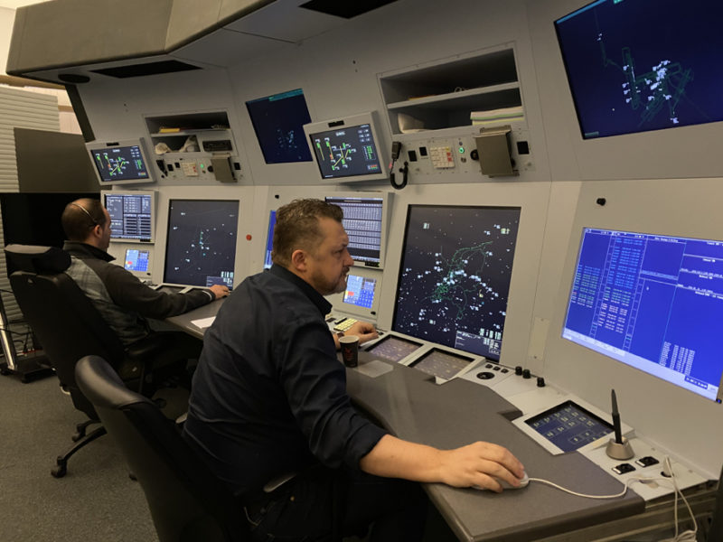 a group of men sitting at a control room with multiple screens