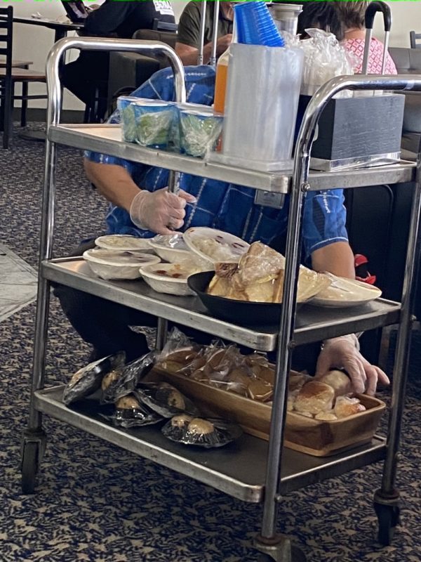 a person in a blue shirt and gloves with food on a cart
