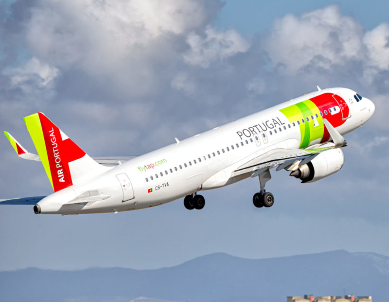 a white airplane with red and green stripes flying in the sky