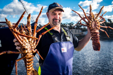 a man holding lobsters in front of water