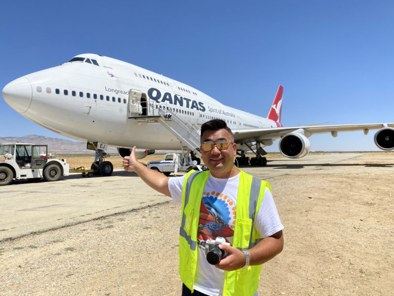 a man in a yellow vest holding a camera in front of an airplane