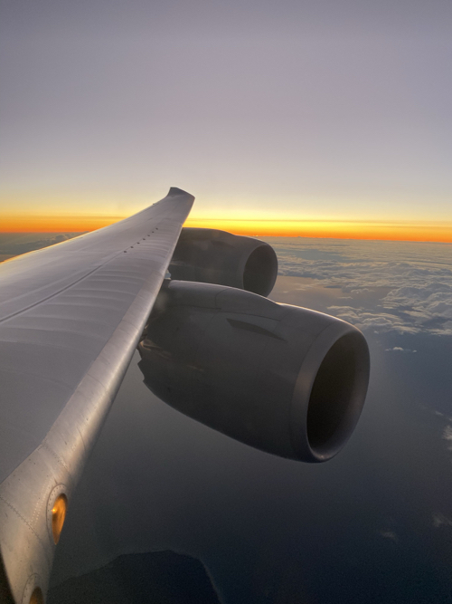 an airplane wing with clouds and sun in the background