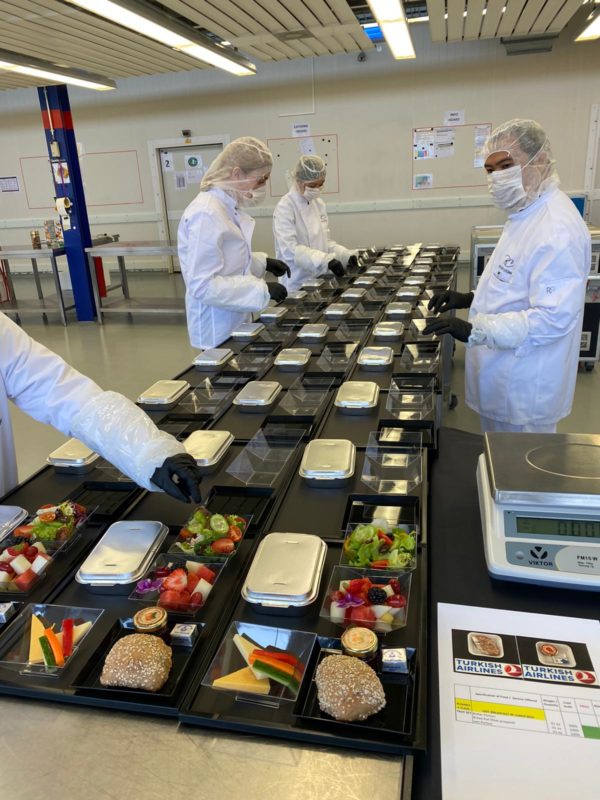 a group of people in white coats and plastic gloves in a room with food
