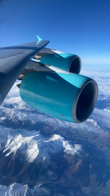 a plane wing with blue engine and snow covered mountains