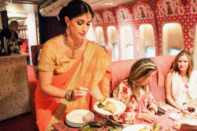 a woman in an orange dress serving food on a plane