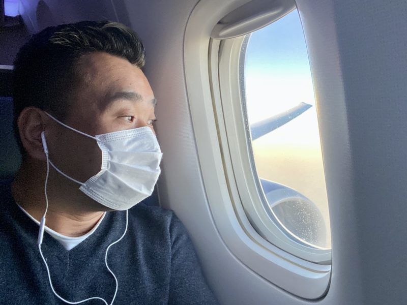 a man wearing a face mask looking out of an airplane window