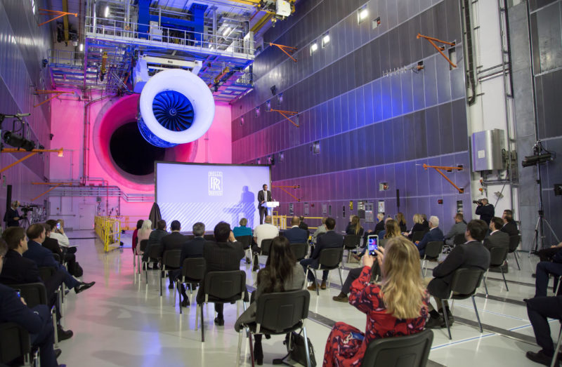 a group of people sitting in chairs in a room with a large jet engine