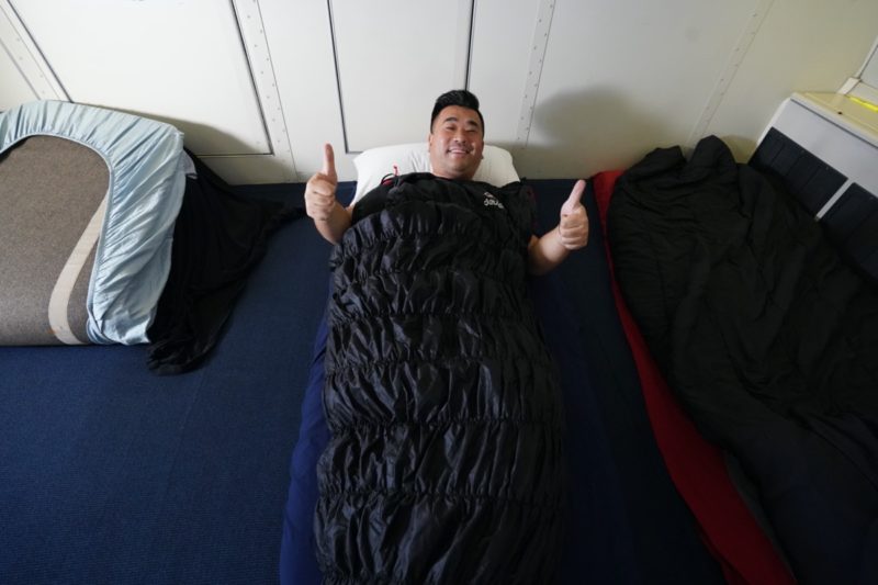 a man lying on a bed with a sleeping bag and thumbs up