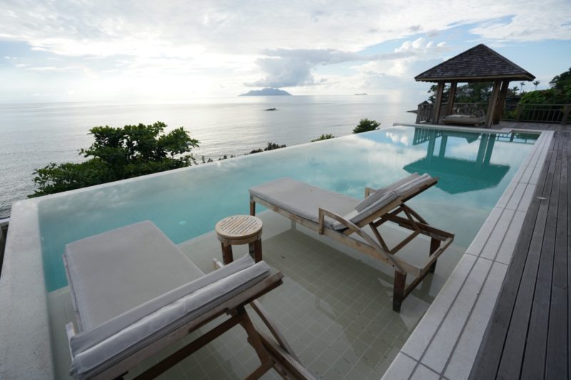 a pool with chairs and a gazebo overlooking the ocean