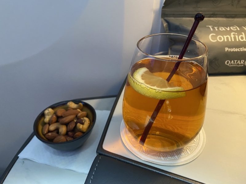 a glass of liquid with a lemon slice and a bowl of nuts