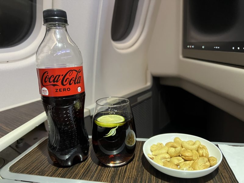 a bottle of soda and a bowl of cashew nuts on a table