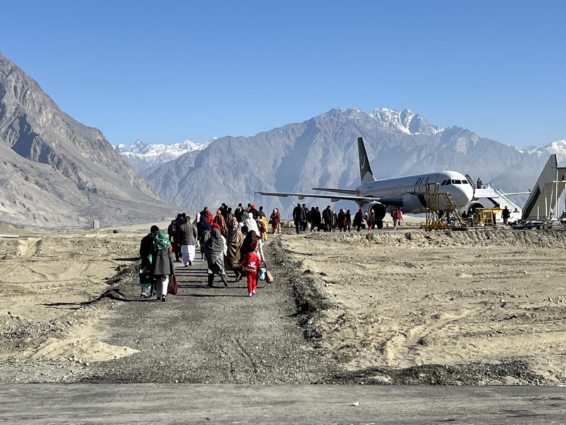 a group of people walking on a runway with a plane in the background
