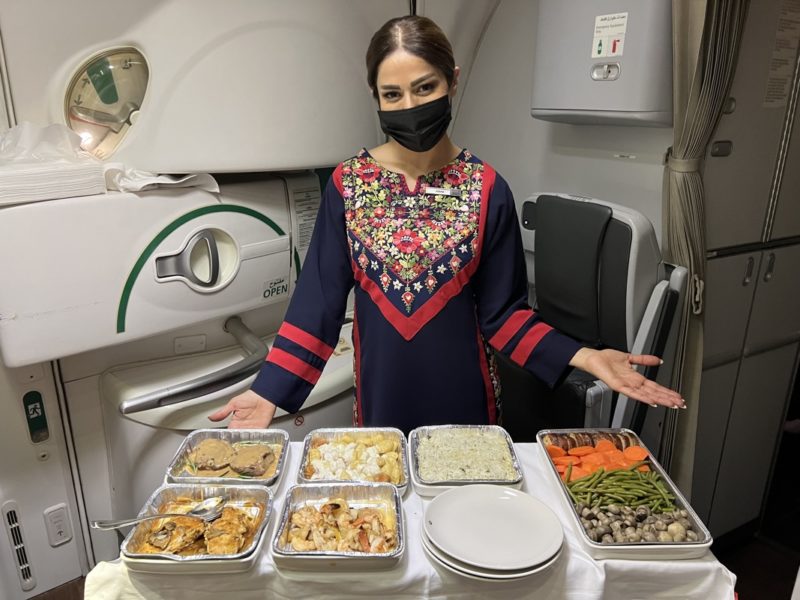 a woman wearing a face mask standing in front of a tray of food