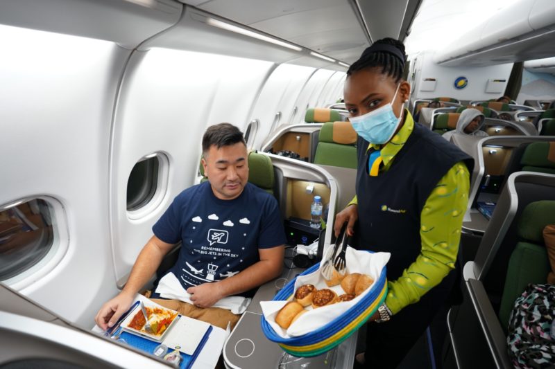 a woman in a mask serving food to a man in an airplane