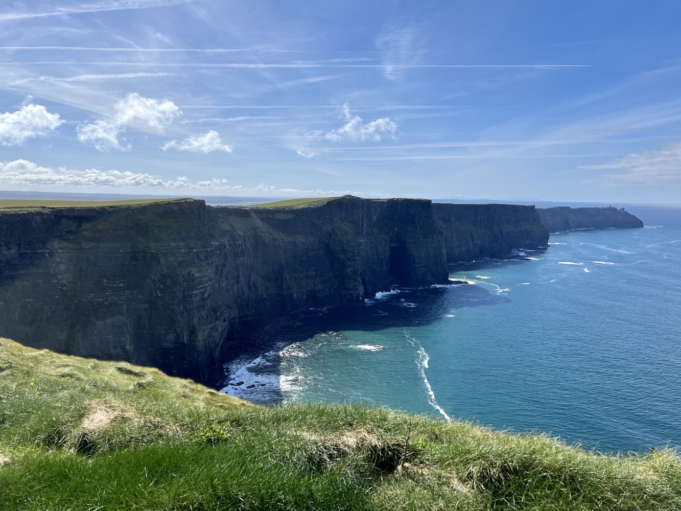 a cliff with water and grass with Cliffs of Moher in the background