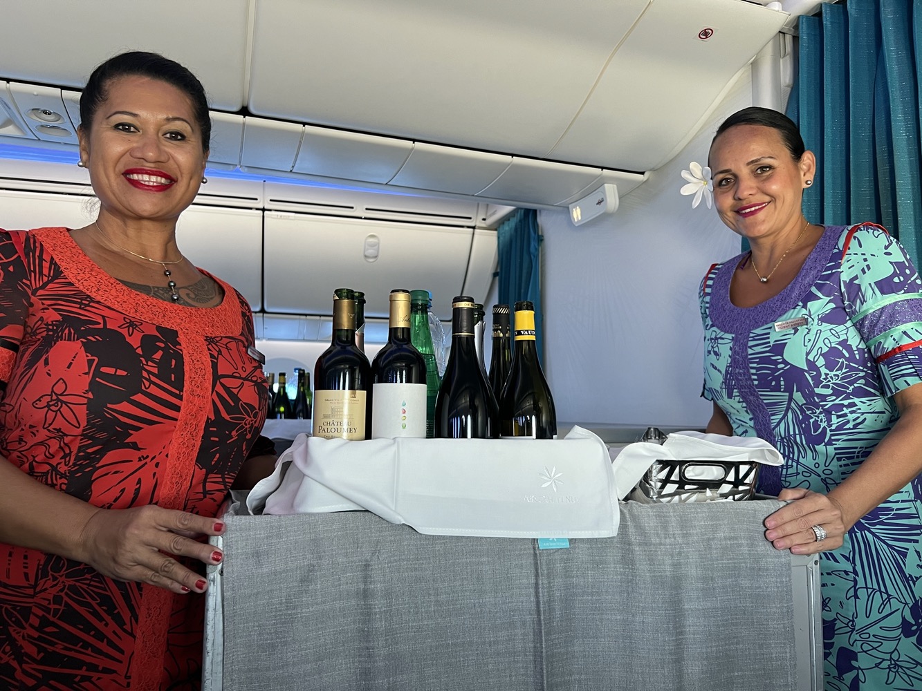 two women standing next to a cart of wine bottles