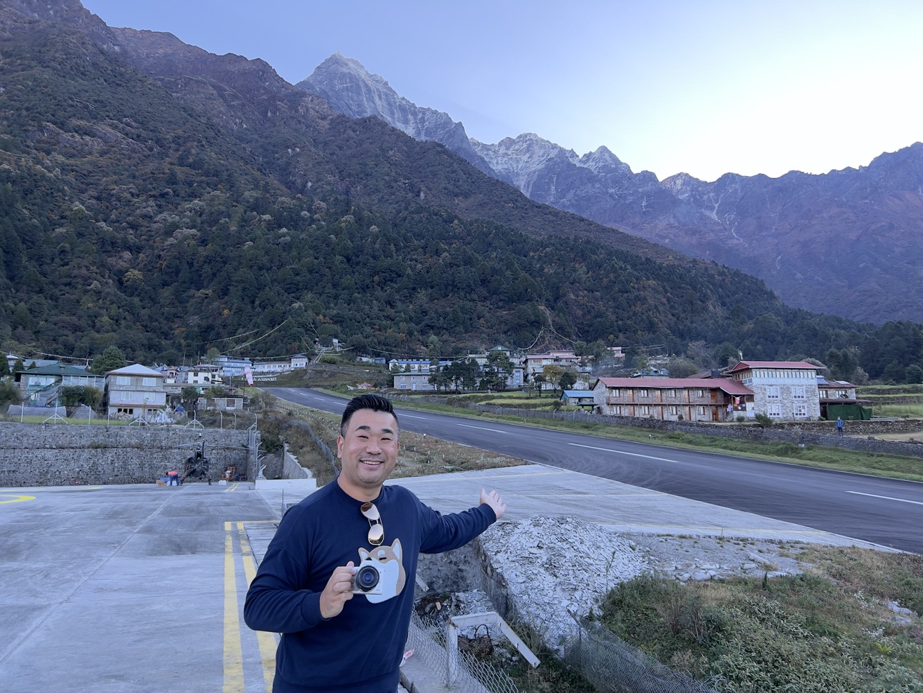 a man standing on a road with a camera in front of mountains