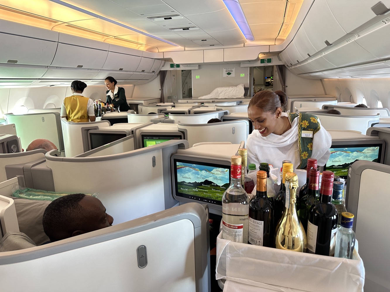 a woman sitting in an airplane with a cart full of wine bottles