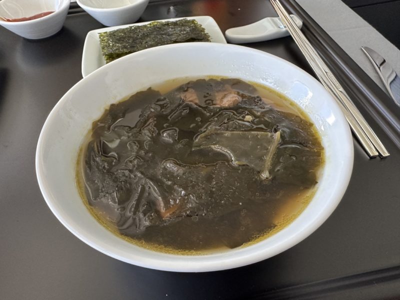 a bowl of soup with chopsticks and a plate of food