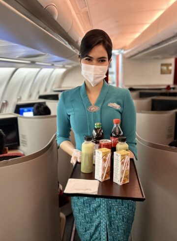 a woman wearing a mask and gloves holding a tray with drinks